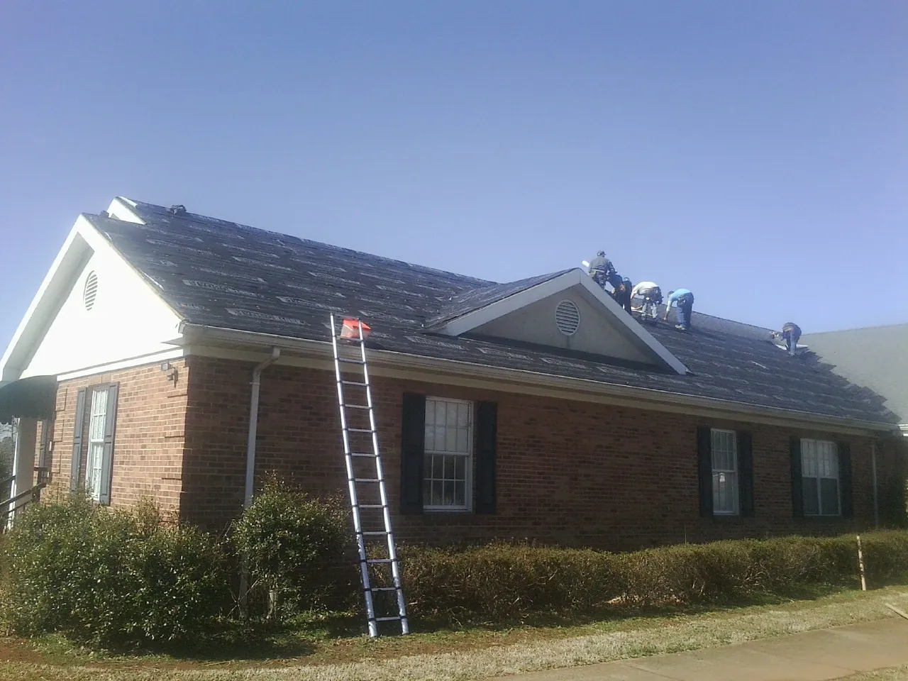 Crew tearing shingles off a brick ranch roof with a ladder set — Emergency Roof Repair work by our crew in Laurel